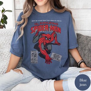 May include: Blue jean t-shirt featuring a vintage comic book graphic of Spider-Man. The design includes the text "The Amazing Spider-Man" in red and white, with Spider-Man in his classic red and blue suit. Additional text includes "Peter Parker Spider-Man."