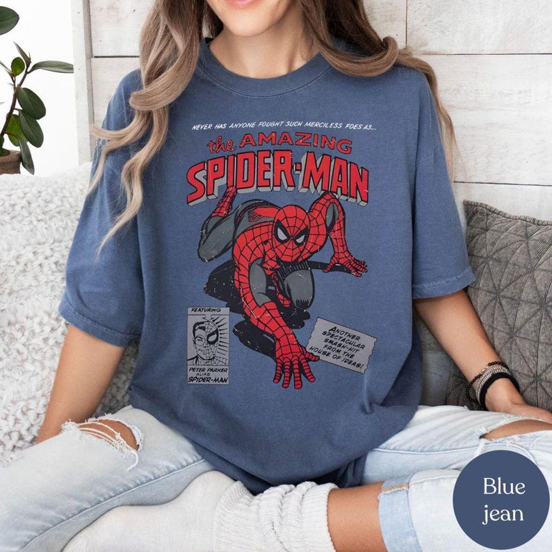 May include: Blue jean t-shirt featuring a vintage comic book graphic of Spider-Man. The design includes the text "The Amazing Spider-Man" in red and white, with Spider-Man in his classic red and blue suit. Additional text includes "Peter Parker Spider-Man."