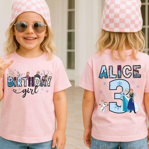 May include: A light pink short-sleeved t-shirt featuring a graphic print. The front displays the text "BIRTHDAY girl" with cartoon characters. The back shows the name "ALICE" above a large number "3" and additional cartoon character graphics.