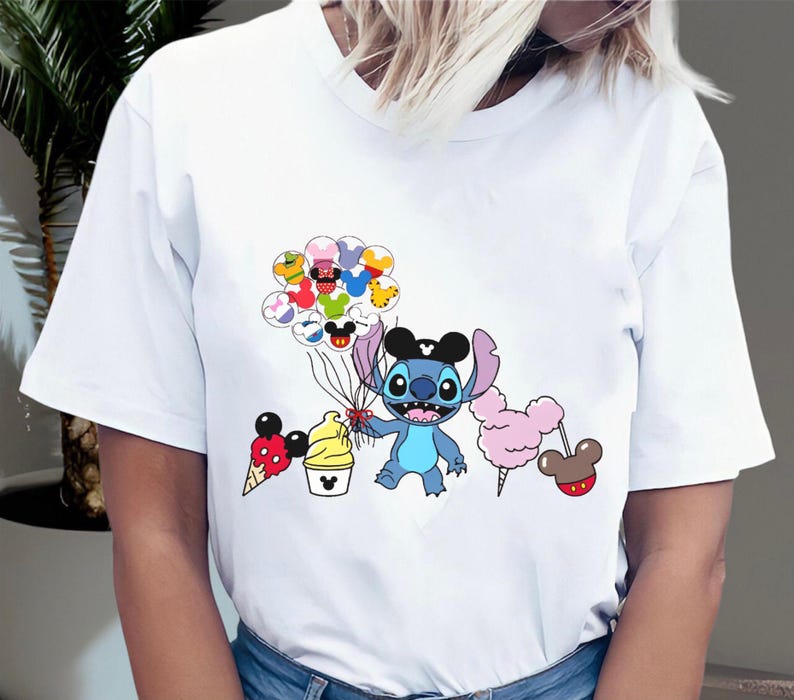 May include: White t-shirt with a blue Stitch character holding balloons with Disney characters on them. The balloons are red, yellow, green, blue, and purple. Stitch is wearing a black Mickey Mouse hat. There is a Mickey Mouse ice cream cone, a Mickey Mouse ice cream cup, and a pink cotton candy on sticks.