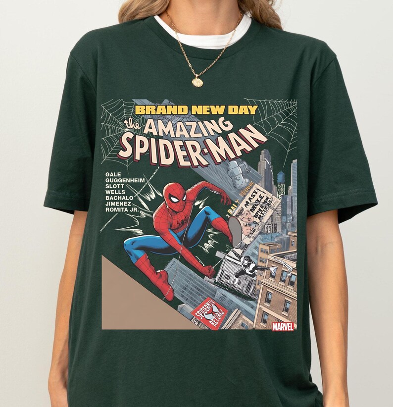 May include: Dark green t-shirt featuring a comic book cover design of Spider-Man. The graphic includes the text "BRAND NEW DAY" and "the AMAZING SPIDER-MAN". The superhero is depicted in a dynamic pose amidst a cityscape.