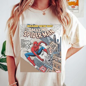 May include: Cream-colored t-shirt featuring a comic book cover design of Spider-Man. The graphic includes the text "BRAND NEW DAY" and "The AMAZING SPIDER-MAN", with Spider-Man in a dynamic pose. The Marvel logo is visible.