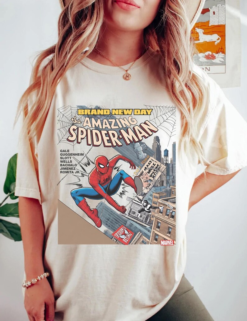 May include: Cream-colored t-shirt featuring a comic book cover design of Spider-Man. The graphic includes the text "BRAND NEW DAY" and "The AMAZING SPIDER-MAN", with Spider-Man in a dynamic pose. The Marvel logo is visible.