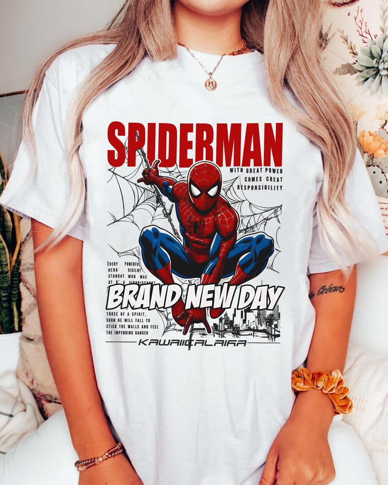 Puede incluir: Camiseta blanca con un dise&ntilde;o de Spider-Man en una telara&ntilde;a, con el texto rojo "SPIDERMAN". El dise&ntilde;o incluye las frases "WITH GREAT POWER COMES GREAT RESPONSIBILITY" y "BRAND NEW DAY".