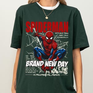 Puede incluir: Camiseta verde oscuro con un dise&ntilde;o de Spider-Man en una telara&ntilde;a, texto "SPIDERMAN" en rojo y las frases "WITH GREAT POWER COMES GREAT RESPONSIBILITY" y "BRAND NEW DAY".