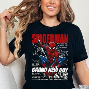 Puede incluir: Camiseta negra con un dise&ntilde;o de Spider-Man en una telara&ntilde;a. El texto "SPIDERMAN" es rojo, con las frases "WITH GREAT POWER COMES GREAT RESPONSIBILITY" y "BRAND NEW DAY" tambi&eacute;n visibles. Cuello redondo.