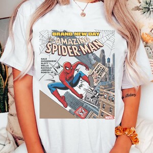 May include: White t-shirt featuring a comic book cover design of Spider-Man in action. The graphic includes the text "BRAND NEW DAY" and "The Amazing Spider-Man" with the Marvel logo.