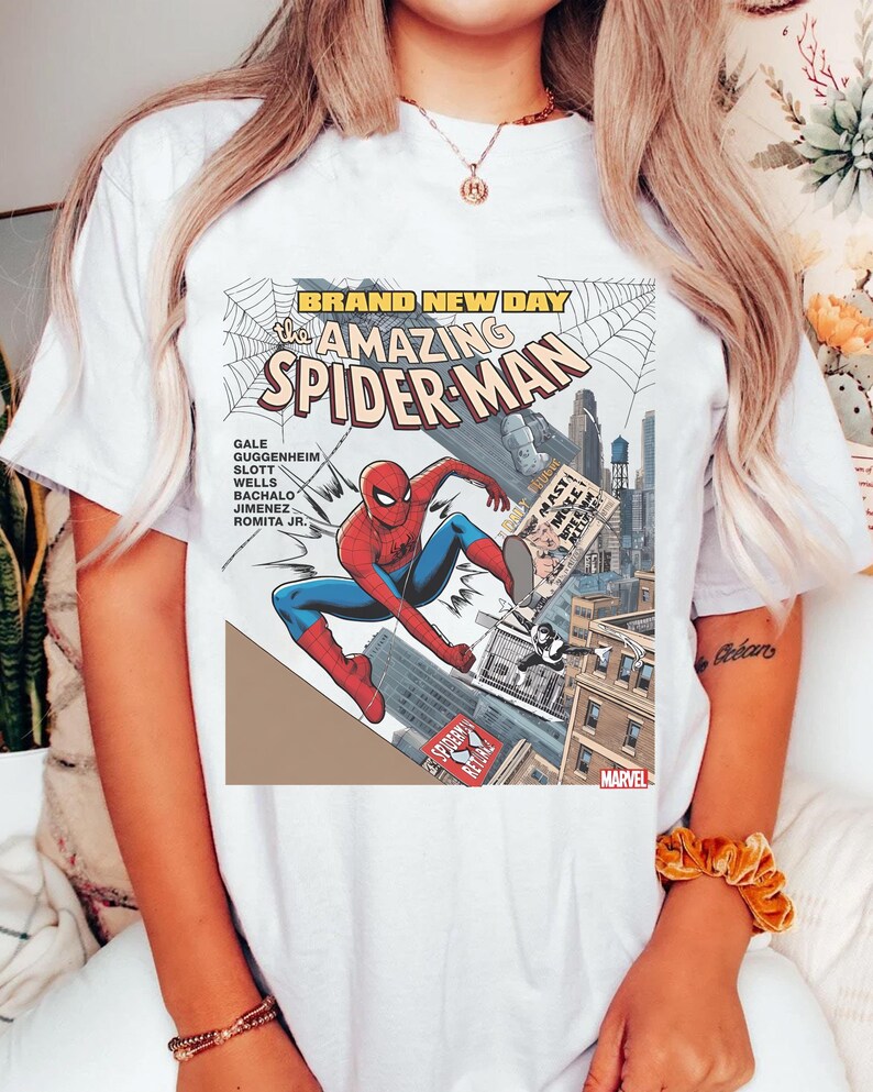 May include: White t-shirt featuring a comic book cover design of Spider-Man in action. The graphic includes the text "BRAND NEW DAY" and "The Amazing Spider-Man" with the Marvel logo.