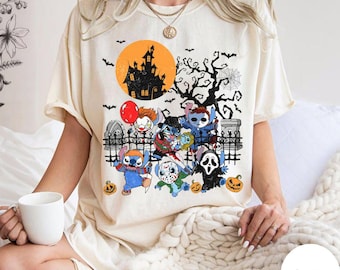 May include: Ivory t-shirt with a Halloween graphic. The design features cartoon characters in horror costumes, a haunted house, bats, and pumpkins. The tee has a crew neck and short sleeves. The colour is described as ivory.