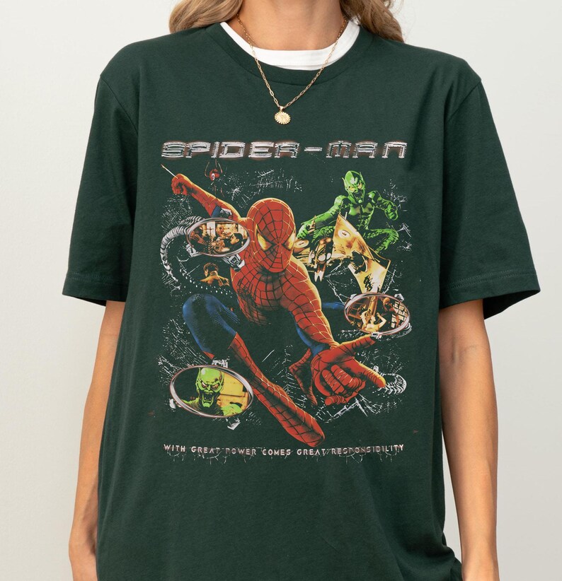 Puede incluir: Camiseta verde oscuro con un dise&ntilde;o de Spider-Man. El dise&ntilde;o muestra a Spider-Man en acci&oacute;n, con las palabras "SPIDER-MAN" arriba y la frase "WITH GREAT POWER COMES GREAT RESPONSIBILITY" abajo. El dise&ntilde;o tambi&eacute;n presenta al Duende Verde.