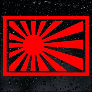 May include: A red rectangular graphic with a central red sunburst design and radiating rays. The design is framed by a red rectangular border, set against a dark, possibly wet, background.