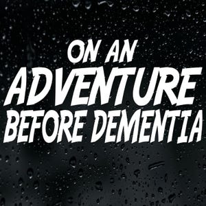 May include: A black decal featuring the white text ON AN ADVENTURE BEFORE DEMENTIA in a bold, sans-serif font. The surface of the decal has a textured appearance with numerous small, scattered water droplets across the entire dark background.