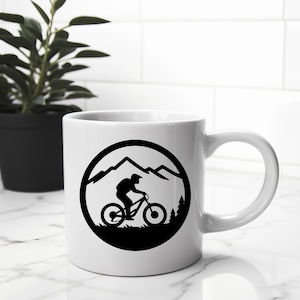 Puede incluir: Taza de cer&aacute;mica blanca con una silueta negra de un ciclista de monta&ntilde;a que recorre un paisaje monta&ntilde;oso dentro de un c&iacute;rculo.