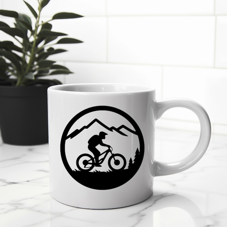 Puede incluir: Taza de cer&aacute;mica blanca con una silueta negra de un ciclista de monta&ntilde;a que recorre un paisaje monta&ntilde;oso dentro de un c&iacute;rculo.