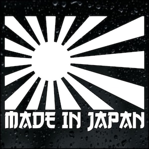 May include: A white graphic of the Japanese flag, featuring a central sun and radiating beams, set against a dark backdrop. The text "MADE IN JAPAN" is displayed below the flag design in a bold, stylized font.