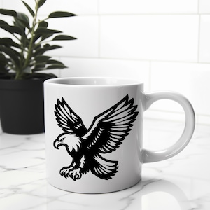 Puede incluir: Taza de cer&aacute;mica blanca con una silueta negra de un &aacute;guila con las alas extendidas. El &aacute;guila mira hacia la izquierda y tiene un pico afilado.