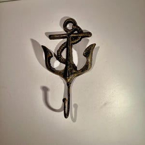 May include: A cast iron anchor hook with a rope detail in a dark bronze finish. The hook is designed to look like an anchor with a rope wrapped around the top.