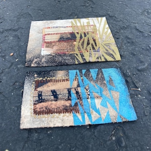 May include: Two rectangular fabric patches featuring distressed textures and stitched borders. The top patch displays gold geometric patterns over black and tan tones. The bottom patch features bright blue geometric shapes over a tan and black base.