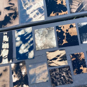 May include: A collection of 12 fabric squares with various bleach-dye patterns in shades of white, black, and brown. The fabric squares are arranged in rows on a gray surface.