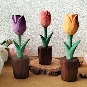 Könnte beinhalten: Drei hölzerne Tulpenblumenskulpturen mit verschiedenen Farbabstufungen. Die Tulpen stehen in kleinen Holzbehältern und sind auf einer Holzbasis angeordnet.