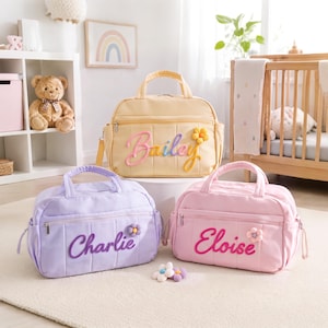May include: Three rectangular quilted bags in pastel yellow, lavender, and light pink. Each bag features a zippered front pocket, two top handles, and a plush flower accent. The names Bailey, Charlie, and Eloise are embroidered in cursive.
