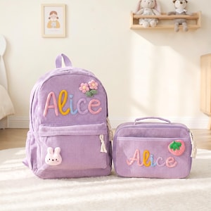 May include: A matching lavender corduroy backpack and lunch bag set. The backpack features the name "Alice" in colorful embroidered letters, a bunny applique, and flower accents. The lunch bag also has "Alice" embroidered and a strawberry applique.