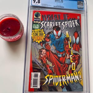Puede incluir: Un cómic calificado en una caja de plástico transparente. La portada del cómic presenta un personaje de superhéroe rojo y azul con el texto "What If... Scarlet Spider Killed Spider-Man?" El cómic está calificado con 9.8 por CGC.