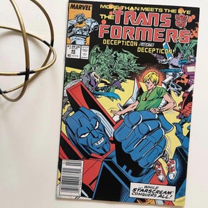 May include: A vintage Marvel Transformers comic book, issue #49, with a colourful illustration of Autobots and Decepticons. The cover text includes "MORE THAN MEETS THE EYE" and "DECEPTICON FIGHTS DECEPTICON!" and a price of $1.00.