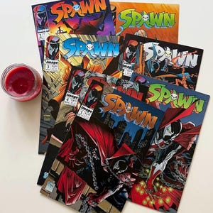 Op de afbeelding: Een verzameling Spawn-stripboeken met de nummers twee tot en met zes, elk met het personage in een rode cape en masker met kettingen. De covers bevatten de titel Spawn in vetgedrukte letters en het Image Comics-logo in de hoek.