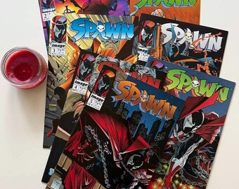 May include: A collection of Spawn comic books featuring issues numbered two through six, each displaying the character in a red cape and mask with chains. The covers include the title Spawn in bold lettering and the Image Comics logo in the corner.