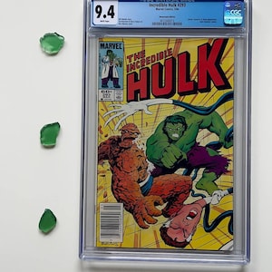 Può includere: Una copia valutata del fumetto Incredible Hulk #293, con Hulk e La Cosa sulla copertina. Il fumetto è racchiuso in una custodia protettiva con un voto di 9,4. Tre pezzi di vetro verde sono a sinistra del fumetto.
