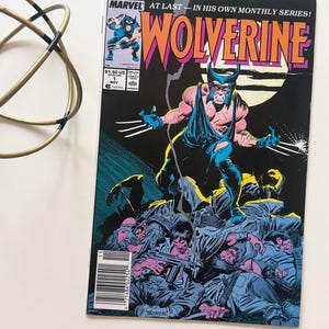 May include: A vintage Marvel comic book featuring Wolverine. The cover art showcases Wolverine in a dynamic pose with his claws extended, set against a black background with the title "Wolverine" in orange and pink. The comic is marked with the price of $1.50.