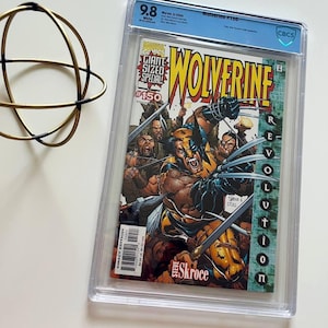 Puede incluir: Un cómic calificado de Wolverine #150, con una calificación de 9.8. La portada muestra a Wolverine con sus garras, rodeado de personajes. El cómic está en una funda protectora transparente. Medidas no aplicables.