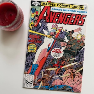 Könnte beinhalten: Ein Vintage-Comic mit dem Titel "The Avengers" mit einer farbenfrohen Actionszene auf dem Cover. Der Comic enthält den Text "Assault on a Mind Cage" und "Ants Attack!" Eine rote Kerze in einem Glas ist im Hintergrund.