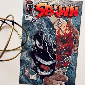 Op de afbeelding: Een comicboekomslag met Spawn, een rood en zwart superheldenpersonage, met een groot, dreigend, zwart-wit beest met een lange tong. De omslag is getiteld "Spawn" en het nummer van het nummer is 37. De comic wordt uitgegeven door Image Comics.