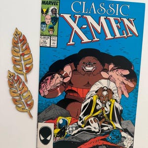 May include: A comic book cover featuring the X-Men. The cover is blue with the title "Classic X-Men" in white. The main image shows the character Juggernaut in brown and red, attacking Storm, who is in a yellow and blue costume. The comic book is from June 1987.