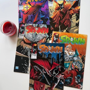 May include: A collection of Spawn comic books featuring vibrant illustrations of the character in action. The covers display the title "SPAWN" in bold lettering, with various issue numbers visible. The comic books are in excellent condition.