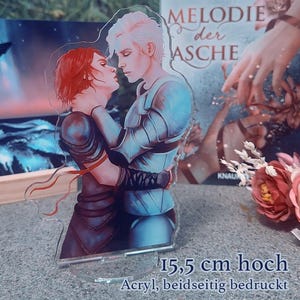 May include: A clear acrylic figure featuring a romantic illustration of two figures embracing. The figures are depicted in armor and dark clothing. The figure is 15.5 cm high and is printed on both sides.