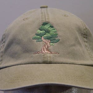 Könnte beinhalten: Eine khaki-grüne Baseballkappe mit einem gestickten grünen Baumdesign.