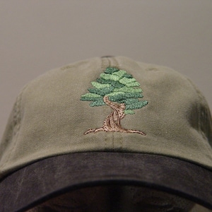 May include: A green and brown embroidered tree design on a khaki baseball cap with a black brim.