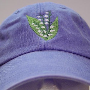 May include: A purple baseball cap with an embroidered lily of the valley design.