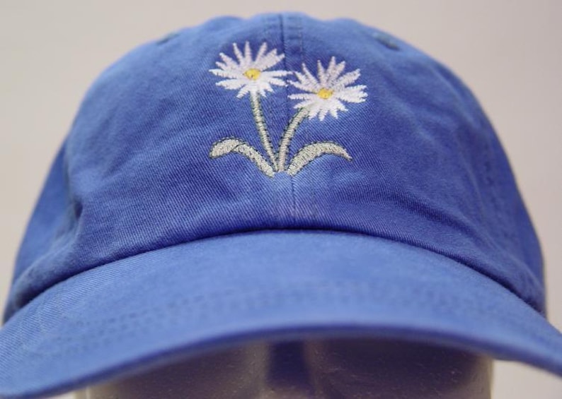 May include: A blue baseball cap with two white embroidered daisies on the front.