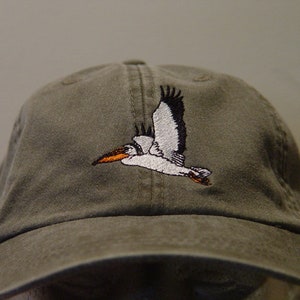 May include: A green baseball cap with an embroidered white pelican in flight.