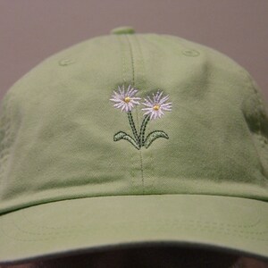 May include: A light green baseball cap with two white embroidered daisies.