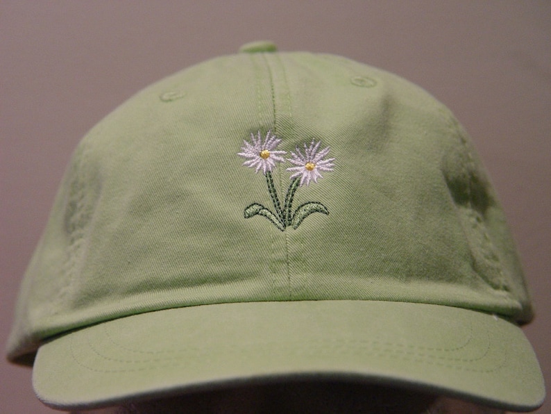 May include: A light green baseball cap with two white embroidered daisies.