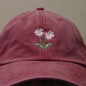 May include: A burgundy baseball cap with two white embroidered daisies.