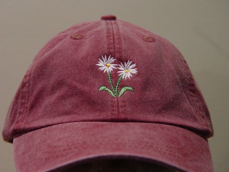 May include: A burgundy baseball cap with two white embroidered daisies.