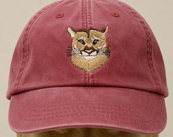 May include: A maroon baseball cap featuring an embroidered cougar face. The cap has a curved brim and an adjustable strap. The cougar's face is detailed with tan and brown thread, with black whiskers and a white mouth.