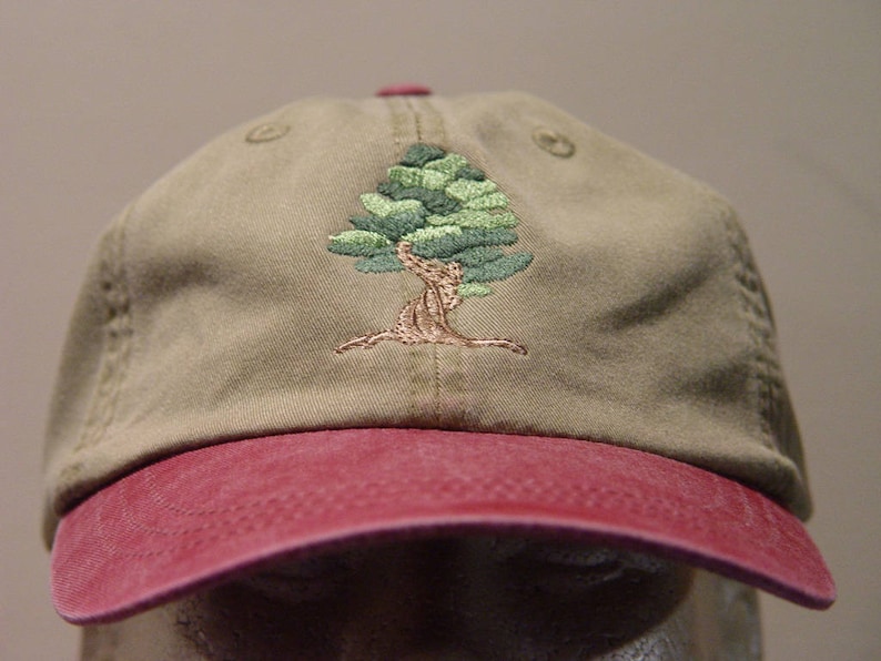 May include: A khaki baseball cap with a red brim and an embroidered green tree design.