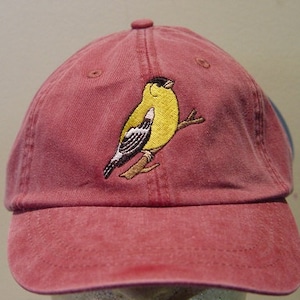 Könnte beinhalten: Eine rote Baseballkappe mit einem gestickten gelben Vogel auf der Vorderseite.
